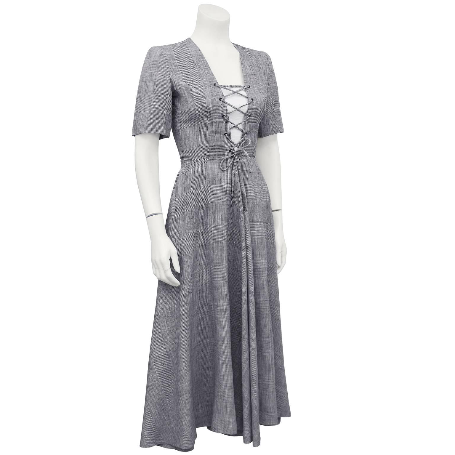 Lanvin gray daydress from the 1970s. The fabric is a miniature houndstooth pattern and the front lacing is constructed from matching material. An elegant silhouette, the short sleeved dress is fitted through the bust and the midi length skirt flares