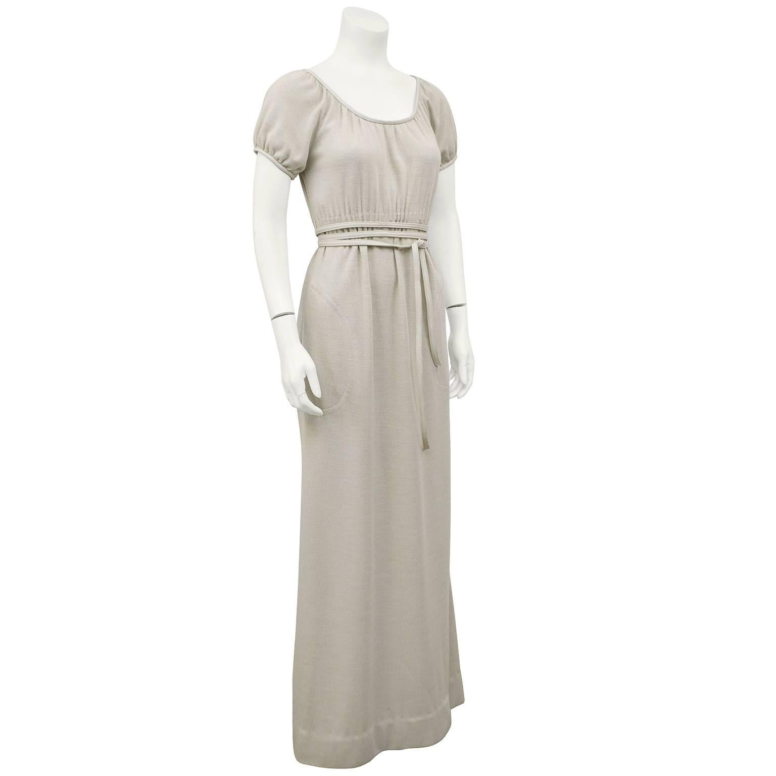 Bonnie Cashin leather trimmed heathered wool jersey gown in cream trimmed in tone on tone leather. The peasant style empire waist gown falls elegantly with some ruching just under the bust and ties with a leather skinny belt. Side slit pockets at