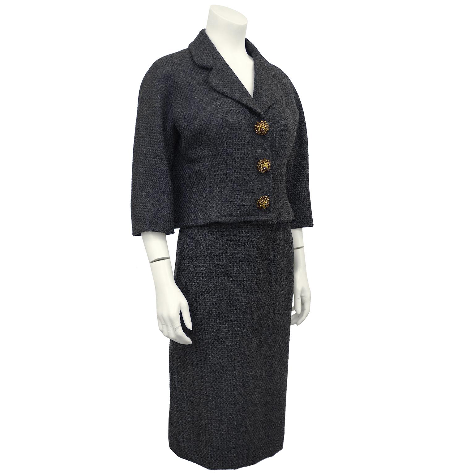 1950s Balenciaga dark gray heavy woven wool boucle skirt suit with oversized jewelled buttons. The cut of the jacket is indicative of 1950s Balenciaga with the wide cropped sleeves and the hem hitting at the high waist. The jewelled accent buttons
