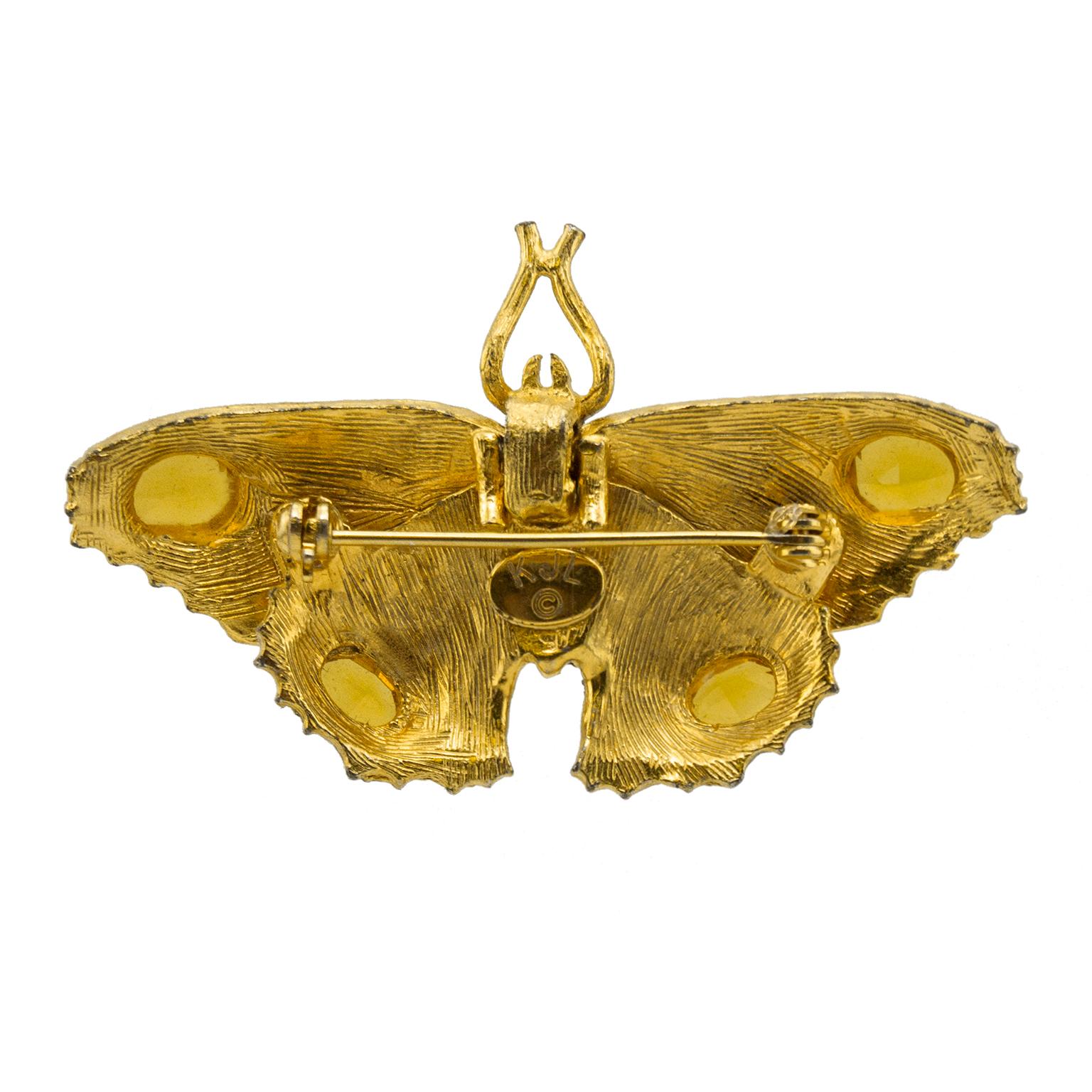 KJL signed rhinestone encrusted butterfly pin from the 1980s. The wings are covered in rhinestones with large oval cut faux yellow stones on the tips. The body is gilded metal with rhinestones in the enter. The eyes are tiny emerald faux stones. The