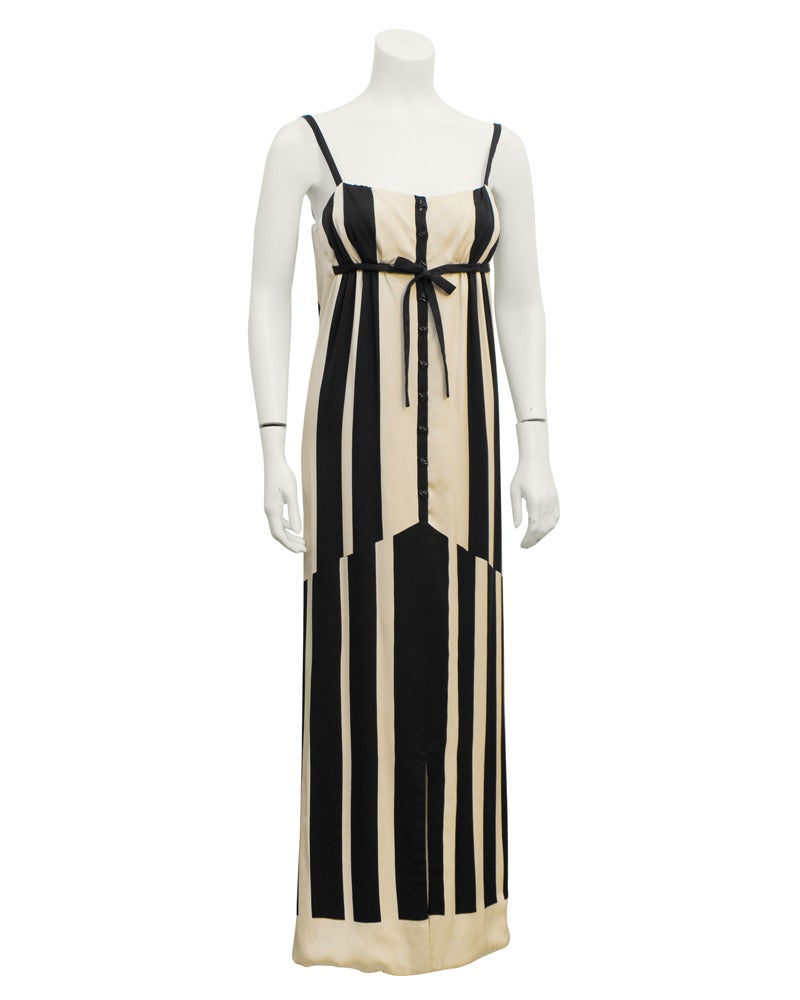 A unique 1960's Pauline Trigere black and white striped silk gown. Features triangle buttons down the front of the dress and a black empire waist tie at bust. Knee length slit up the front seam. In good vintage condition, very minor pulling