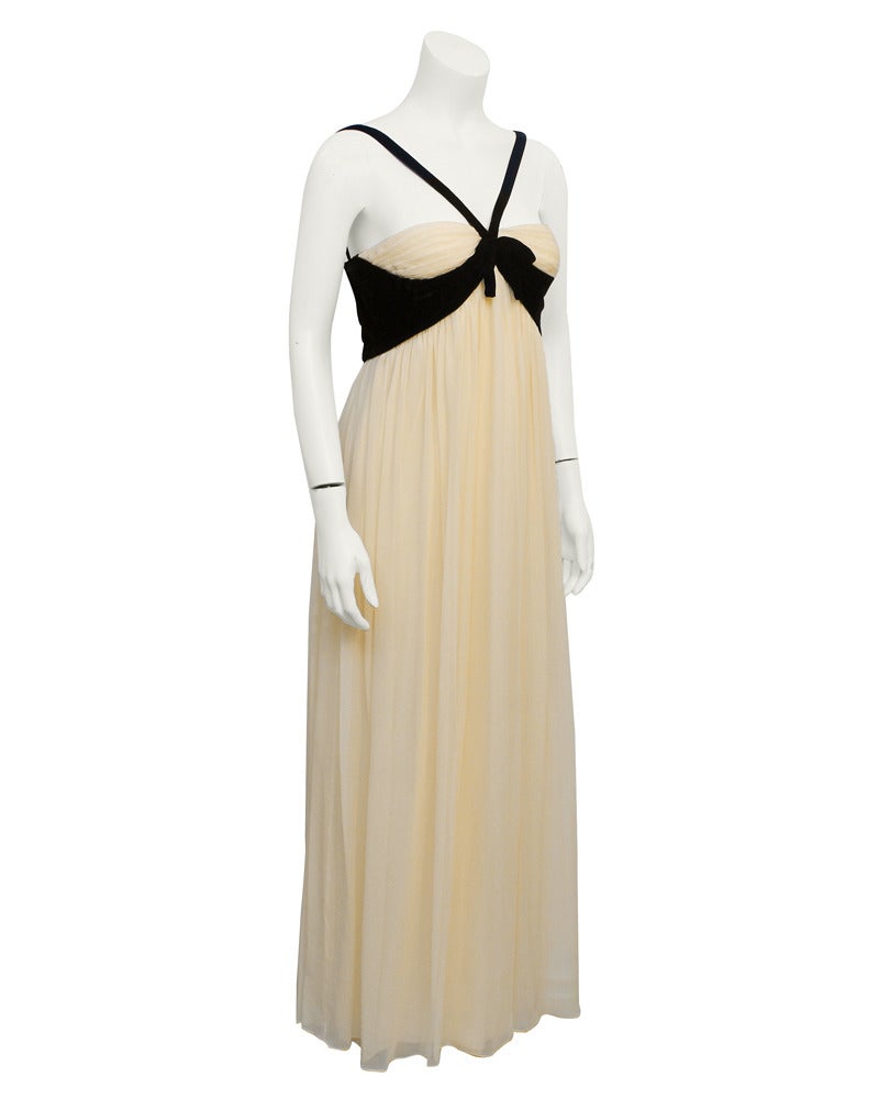 Etherial cream chiffon and black velvet Sarmi empire waist gown from the 1960's. Black velvet straps come around the shoulder and cross, meeting mid chest, embellished with a bow. Velvet accent continues under bust and around back. Lined in white