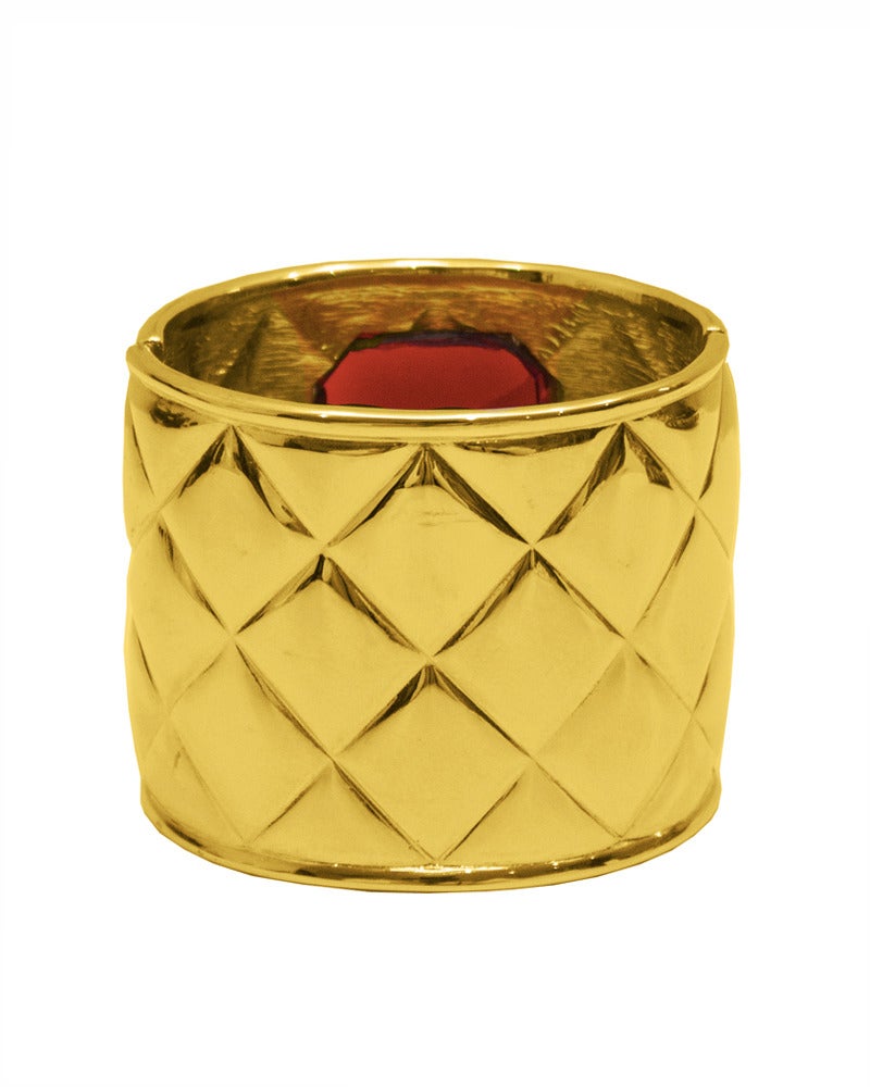 Gold-tone metal quilted Les Bernard cuff circa late 1980's - early 1990's, as evidence by the small VO marking on inside of cuff. Large red poured glass stone in centre of cuff. Excellent condition, very little scratching.