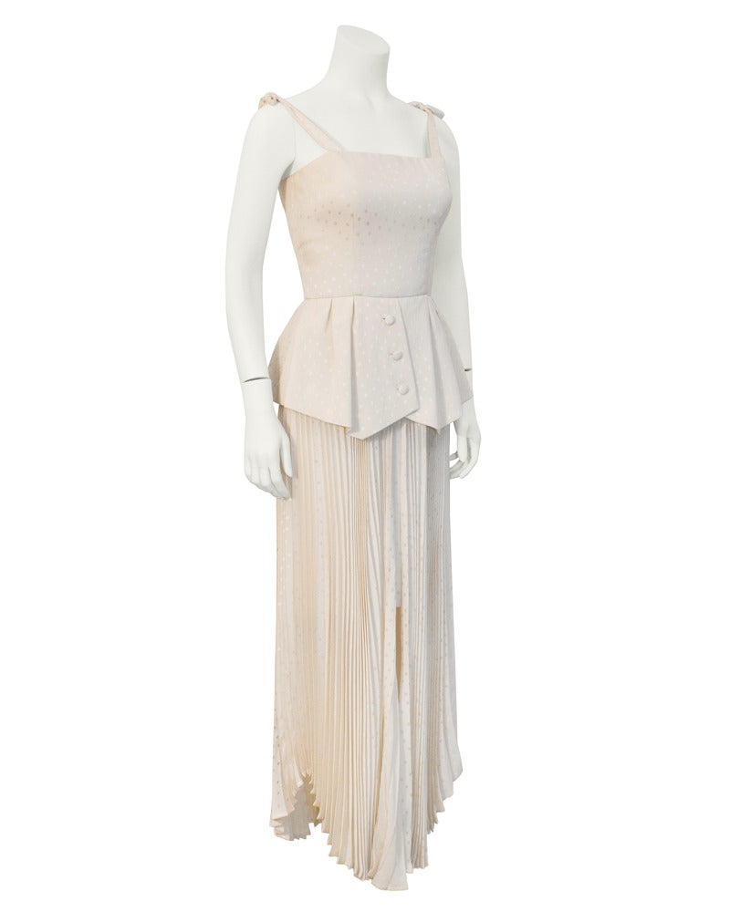Circa 1980's Andre Laug featuring adjustable straps, a fitted bodice, a large peplum and a pleated, hanky hem skirt with a large front slit and a short under skirt. Peplum has inverted pleats 3 buttons down the front. Beautiful off-white silk