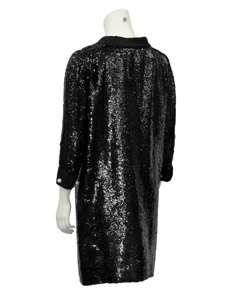 This 1960s black dress is comfortable and elegant at the same time. Covered in black sequins with a black satin collar, cuffs and band down the front covering buttons. Finished with rhinestone buttons on the cuffs. Very forgiving loose look fit. In