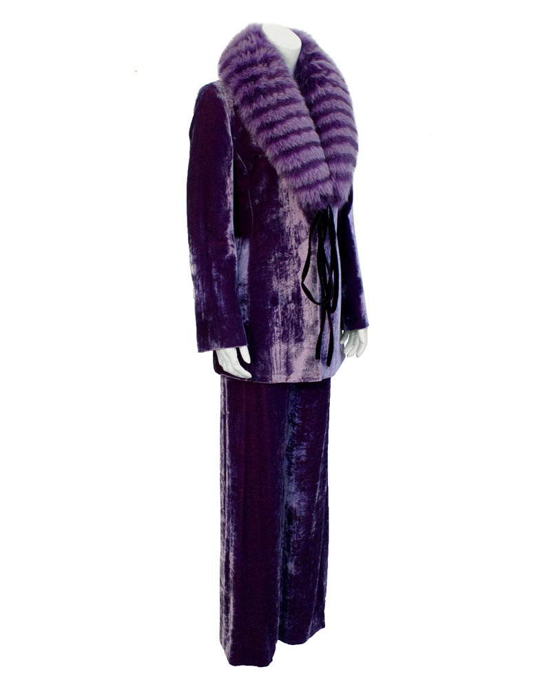 1980's purple crushed velvet Ferre pantsuit with a matching dyed purple fox fur collar. Suit features a long blazer and wide leg trousers. The fur stole fastens with a black velvet tie at the front. Interesting and eye-catching piece. In excellent