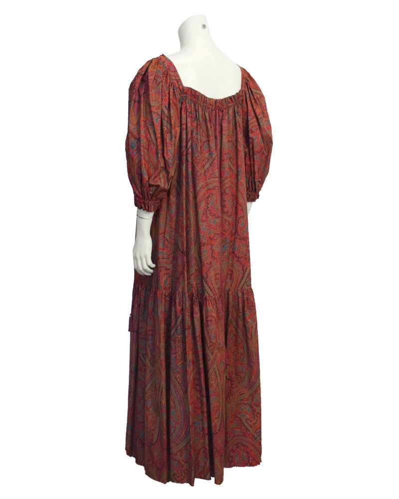 1970's red cotton paisley Saint Laurent Rive Gauche peasant style hostess gown. Paisley print includes tones of red, orange, green and blue. Two woven and twisted strings attached at the shoulders can be tie however you desire. Gathered at cuffs,