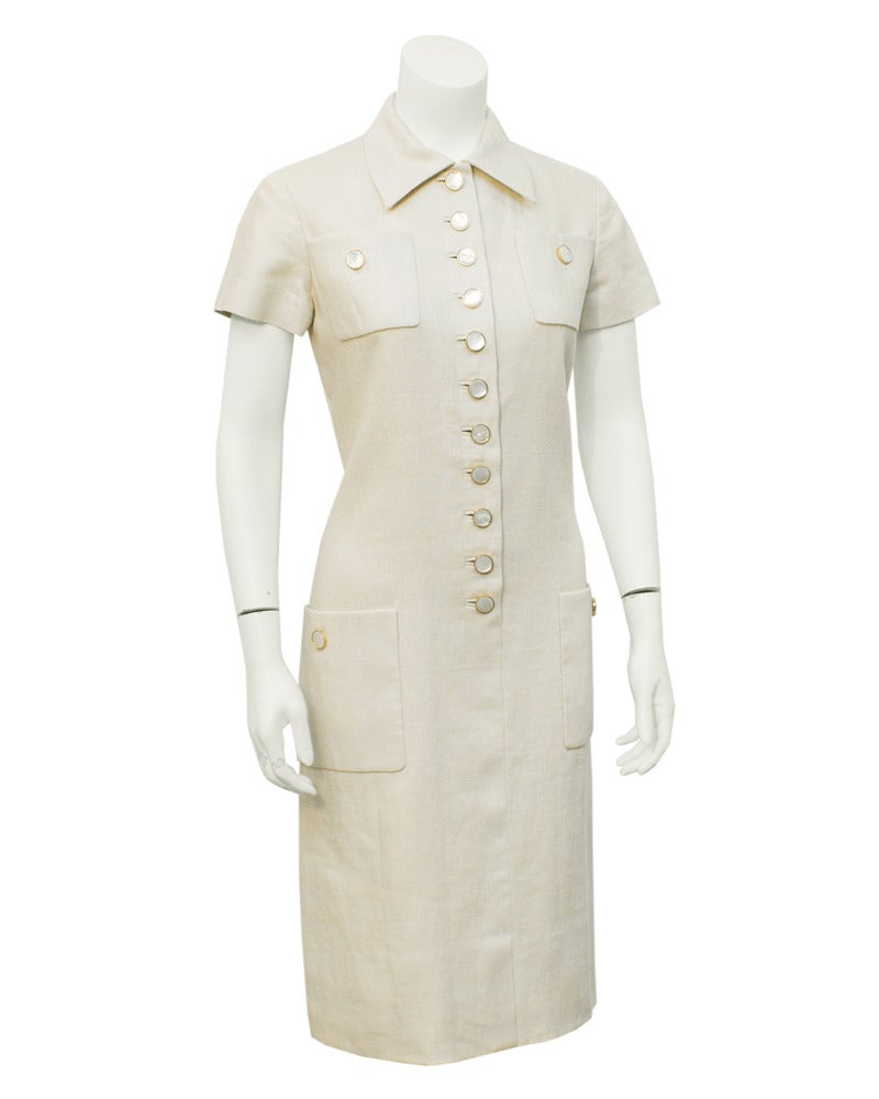 1960's Norman Norell cream linen short sleeve day dress. Two flat front pocket at bust and two at hips. Beautiful white mother of pearl buttons in gold tone casing on pockets and down the front center seam, ending at the hips. Fully lined in