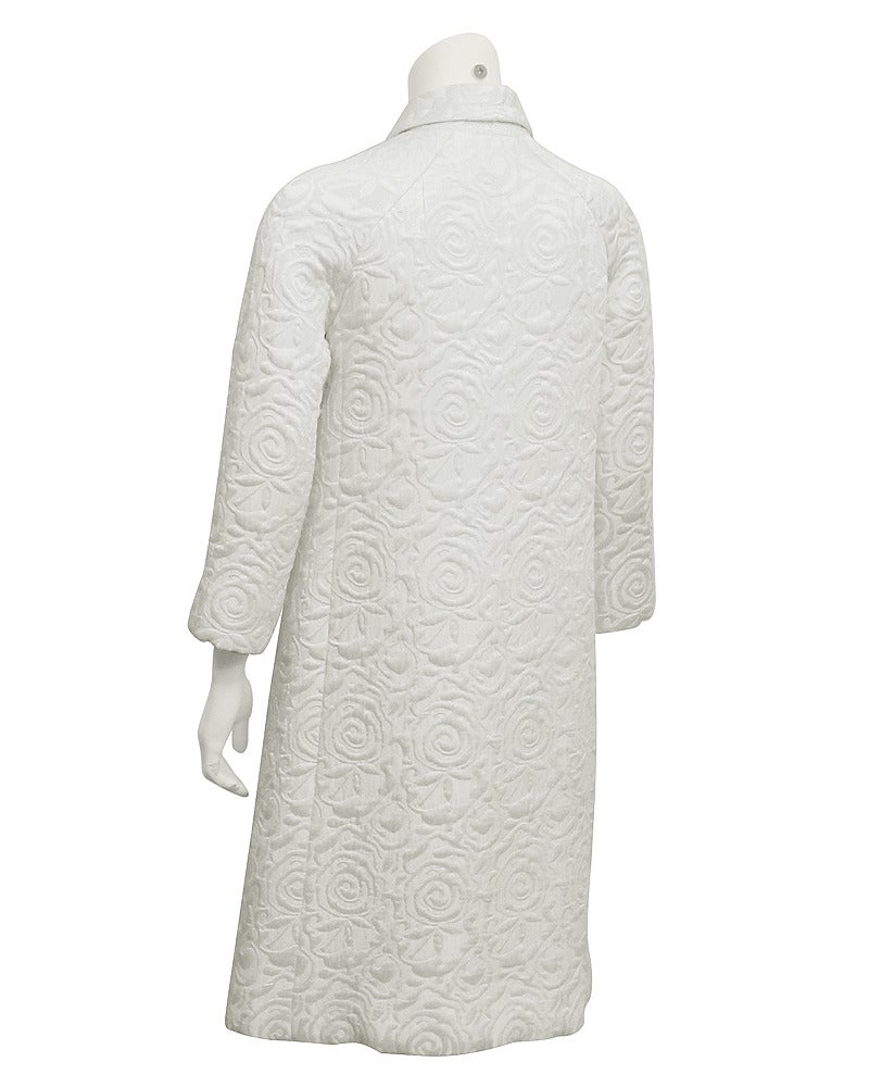 Magnifique ensemble manteau, robe des années 1960 conçu par le label français Ulrique. Les trois pièces sont coupées dans un brocart de laine blanc monochrome. Le manteau présente des manches de type bracelet, un nœud au col et trois boutons ronds
