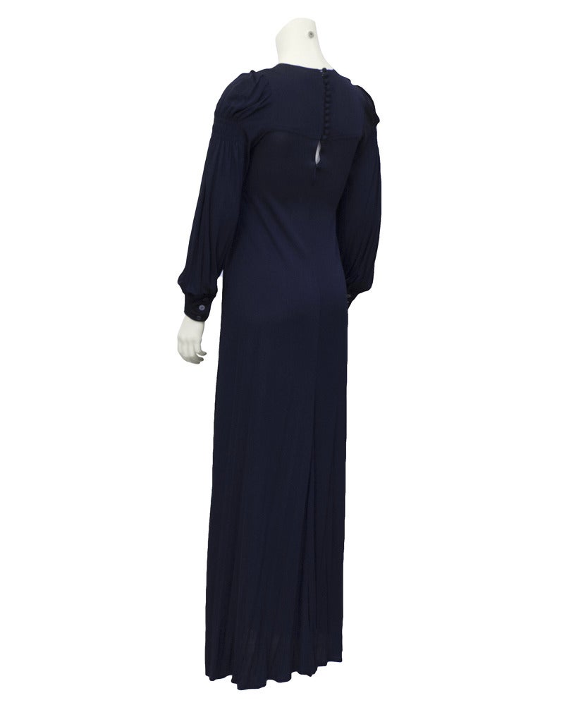 1970's navy blue, long sleeve polyester jersey gown with a yoke and hand smocking through the shoulders and bust. Cuffs have two fabric covered buttons and the sleeves are over sized with a soft drape. Invisible zipper and ten buttons up the back.