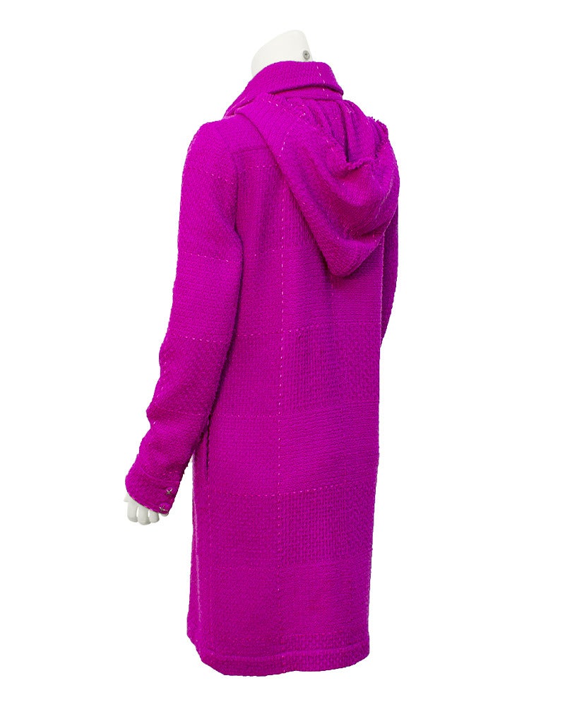 Fuchsia wool blend Chanel boucle coat from Fall 2007 with an attached hood. The coat has a stitched windowpane pattern in a lighter pink thread and the buttons are covered in the matching fuchsia fabric with gunmetal X's on top. Pockets on the