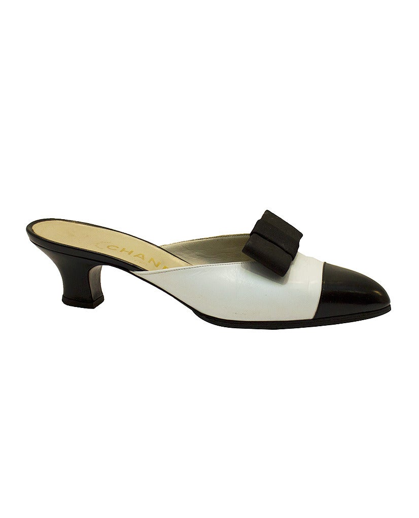 White and black 1990's Chanel leather mules. White leather body with a black cap toe and removable black bow clips. Classic Chanel markings on the heel and sole. Perfect way to complete any chic resort or vacation look. Timeless neutral color