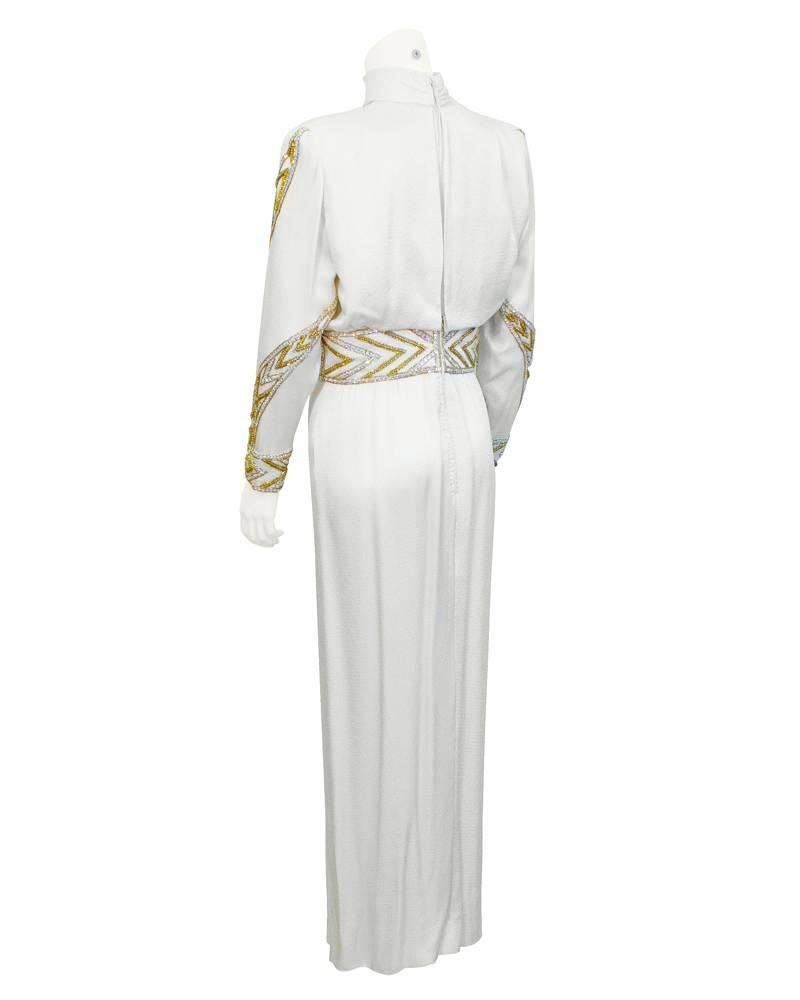 1980's White satin crepe, long sleeve, turtleneck Bob Mackie gown embellished with gold and silver beading on the arms and waist. Beading spirals down both arms and creates the illusion of a tied belt at the waist. In excellent vintage condition.