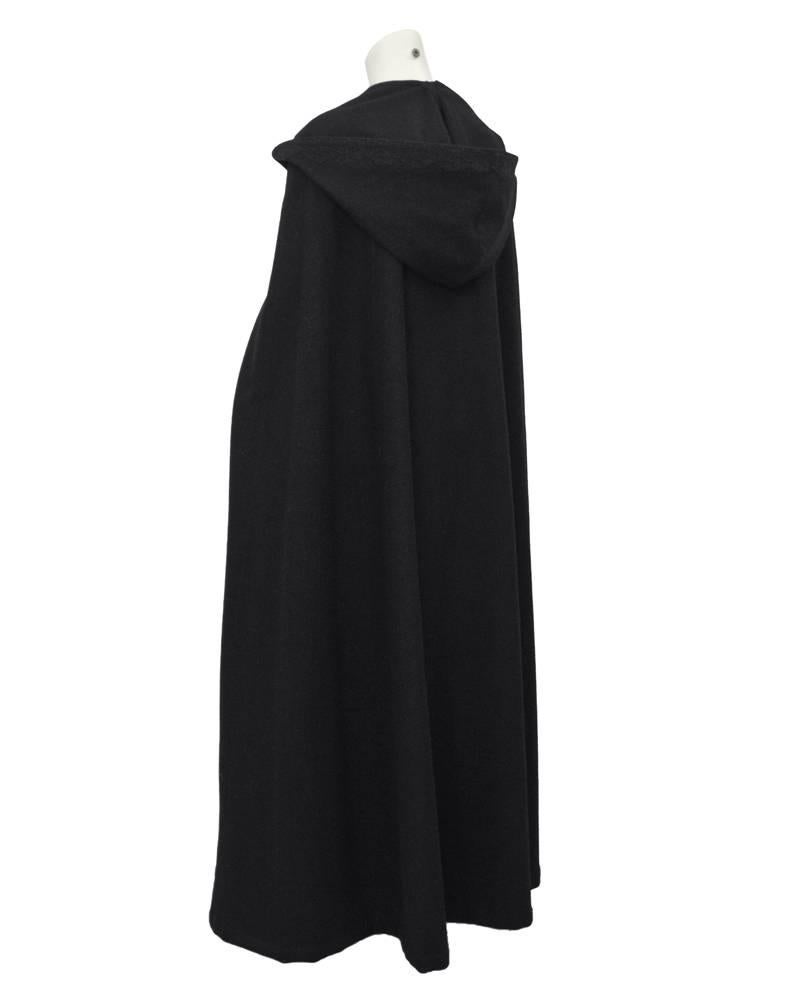 Long black wool hooded cloak dating from the 1960's. Ornate embroidered trim with black silk thread. Four large black hook and eye closures at bust. Excellent vintage condition. Dramatic and versatile. Generous fit from 4-12 US