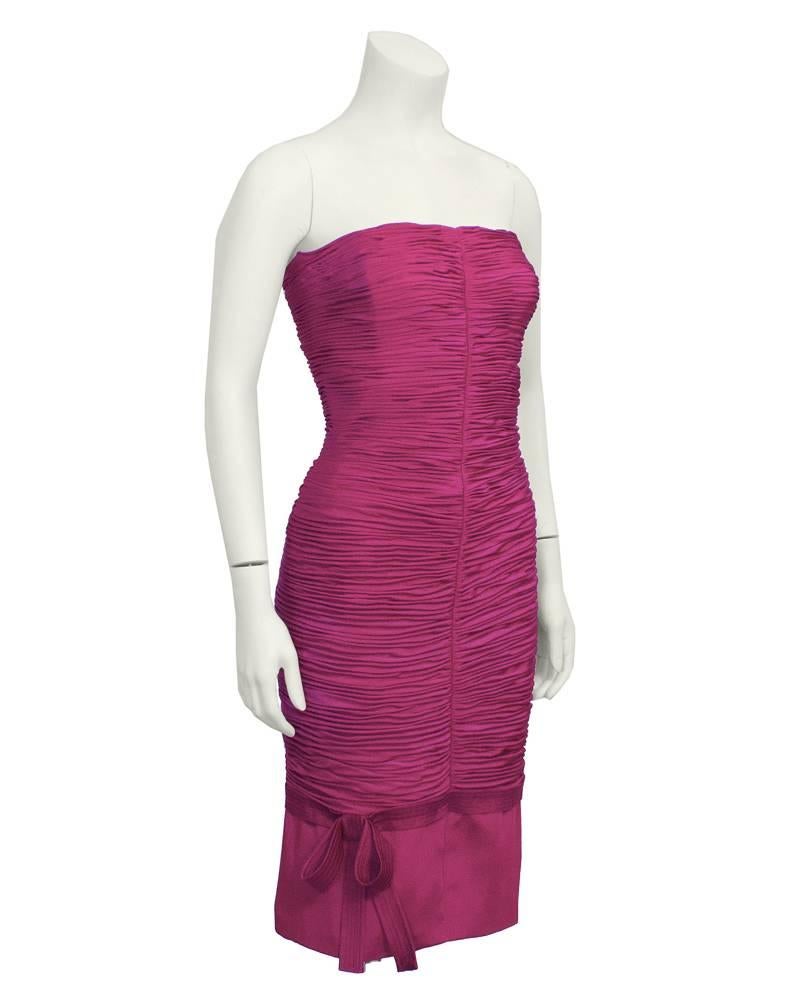 1990's Gianni Versace magenta form-fitting strapless Wiggle dress. Ruched silk with a centred vertical seaming creates a flattering body-conscious fit. Bow detail on bottom adds feminine touch. Back zipper with a hook closure. Fully lined with silk.