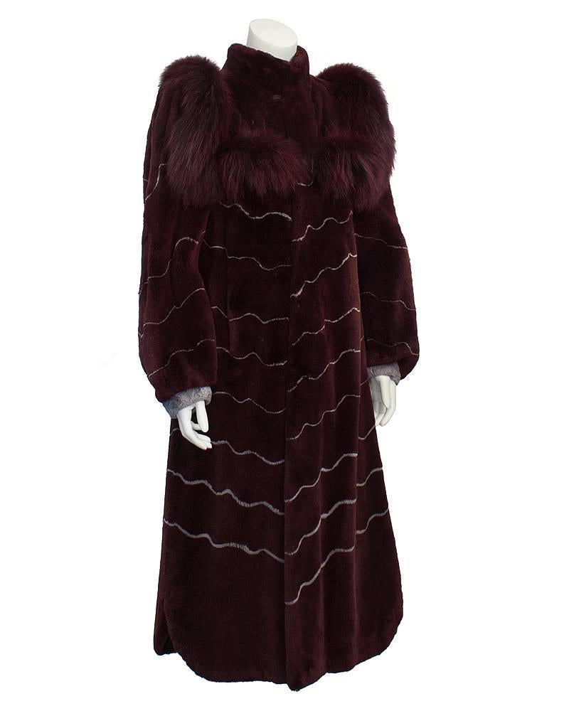 Chic 1970s artist designed burgundy shaved fur coat (mink) with dyed to match fox fur trims. Exaggerated fur trim along the shoulders and bodice, with grey wavy inlaid design. Slightly gathered sleeves with grey fur cuffs. Above ankle length with