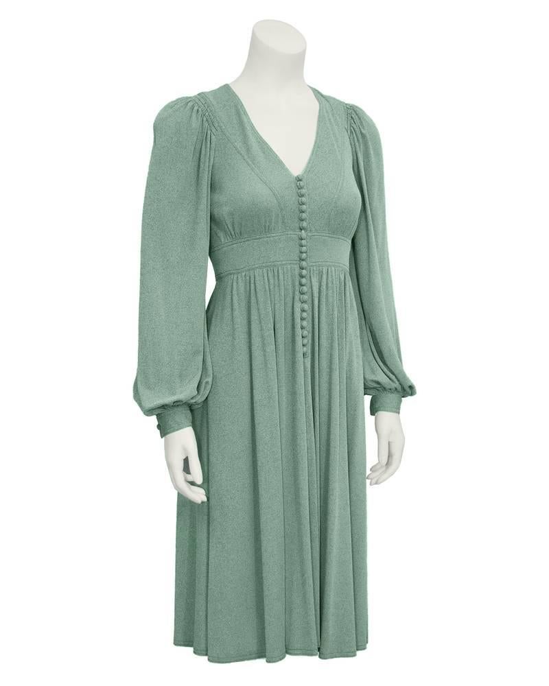 1970's British designer Jean Muir's heathered green knee-length day dress. Empire style waist line with soft draped pleats, pin tuck stitching, V-neck and loop buttons down center. Sleeves are gathered at shoulder and wrists, with buttons on each