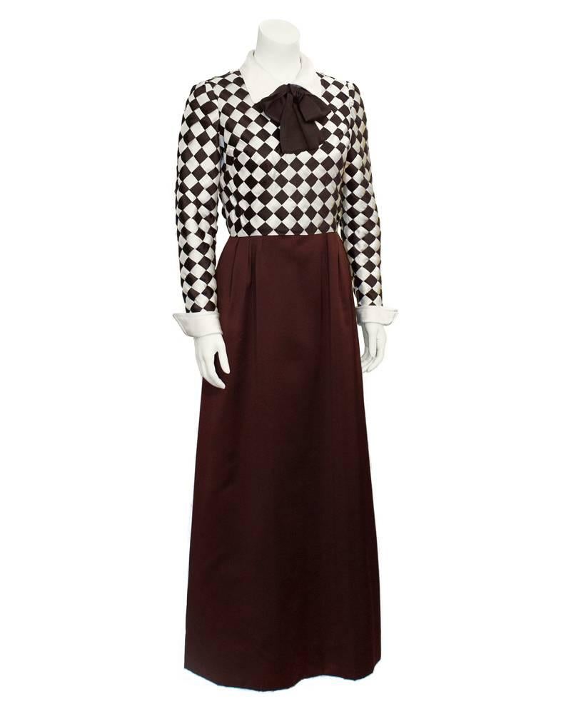 Fabulous Harry Algo brown and cream satin shirtwaist style gown from the 1960's. Upper bodice with a silk cream collar and a large brown bow. Woven satin ribbon on bodice creates checkered pattern. Three fixed pleats at each hip. Back zip closure.