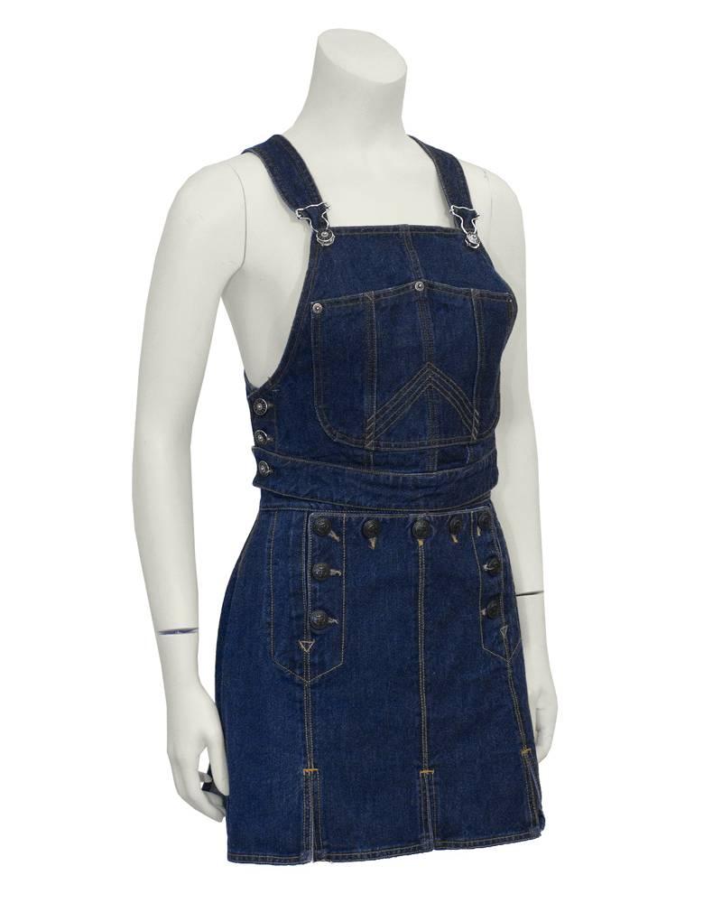 Unusual Jean Paul Gaultier denim 2 piece set from the early 1990's.  Cropped bib style overall top with adjustable shoulder straps and silver hardware. Three button closure on each side with custom buttons. Skirt has sailor-style drop flap with