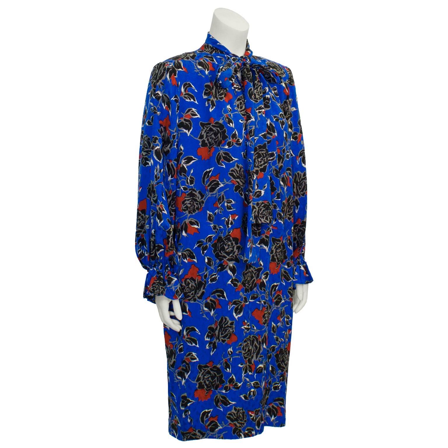 Amazing Yves Saint Laurent electric blue silk jacquard long sleeve dress  with sweet neck tie from the 1980s. Features a semi abstract rose pattern with notes of black, white, red and grey. Padded shoulders, and a v-neck with a long tie collar.