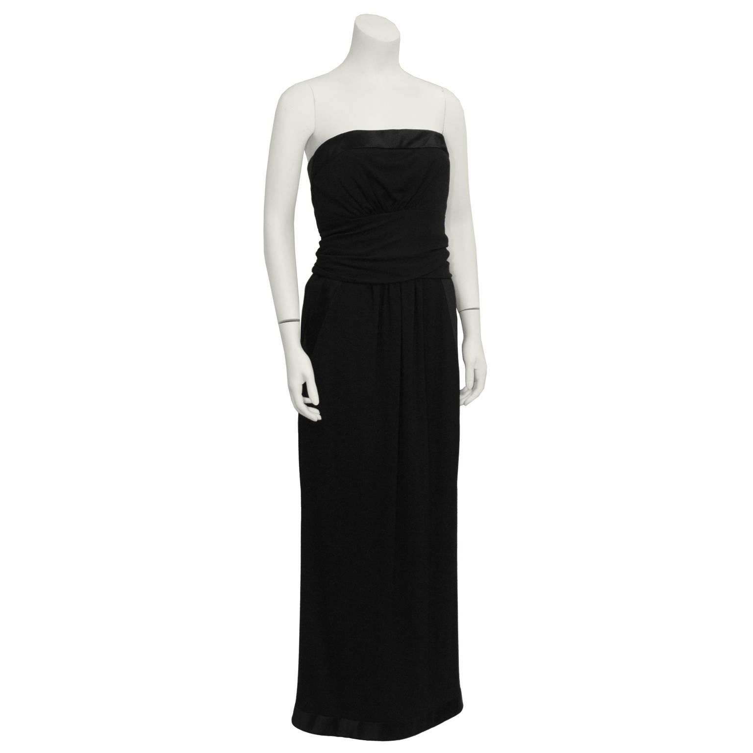 1980's Chanel black strapless gown. Features silk satin band around the top and the hemline. Belted around waist, with slight gathering on bodice and skirt. Side slash pockets. Back of the column skirt has three vertical buttons on the bottom.