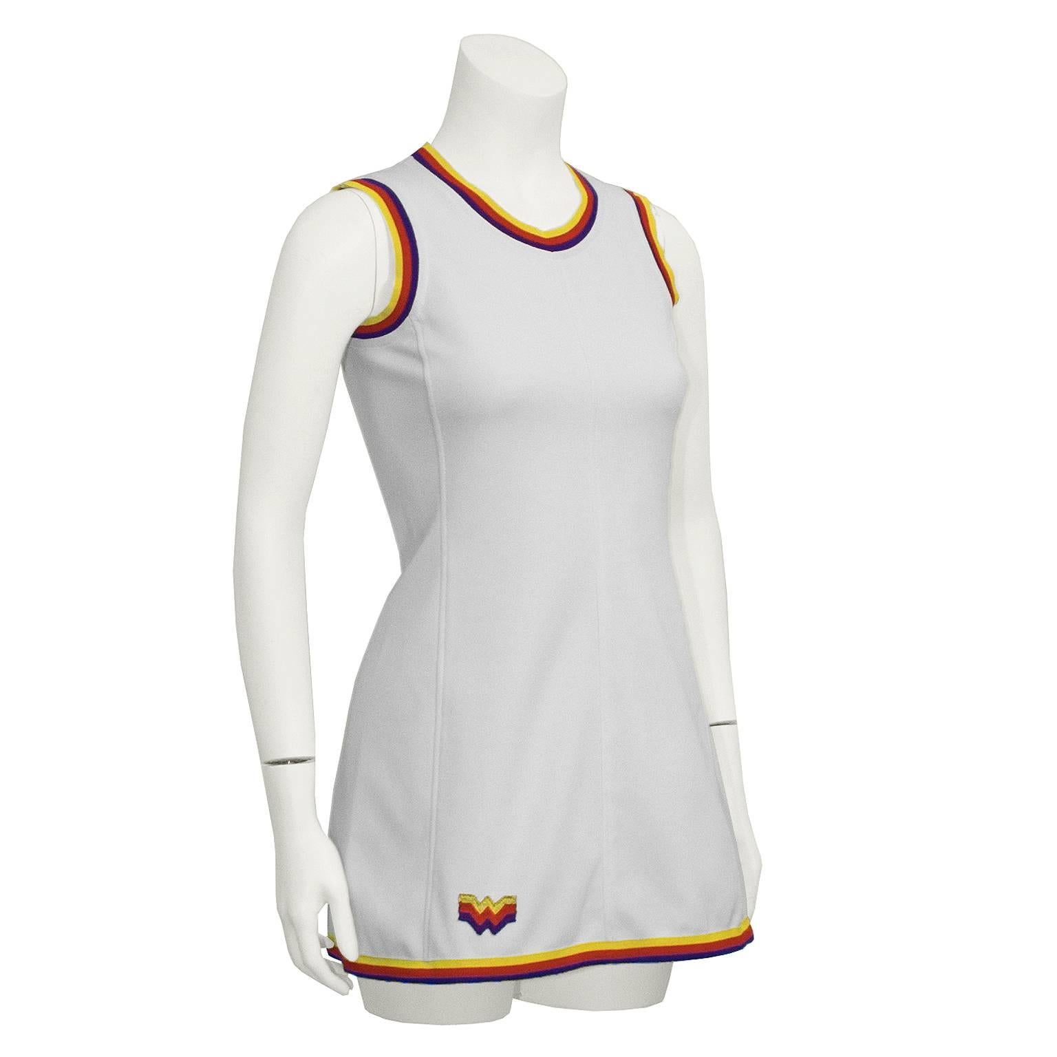 Adorable 1960's tennis dress from German athletic wear brand Bogner. Sleeveless mini-dress is white polyester, with ribbed trimming in yellow, red, and blue horizontal lines. Vertical seaming on front adds flattering figure accenting shape.