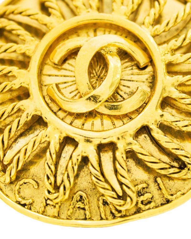 Gold-tone Chanel pin from the fall 1994 collection. Gold plated metal in a rope motif outlines a sun emblem with the classic Chanel CC logo in the center of the sun. The rope motif also spells out CHANEL at the bottom of the pin. The back is a