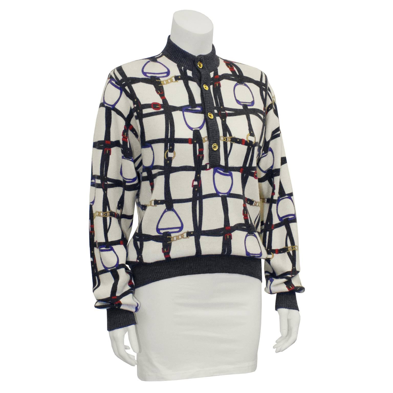 Adorable Celine cashmere sweater with equestrian print from the 1970's. Sweater has charcoal ribbed trim, and the print is a cream background with notes of charcoal, red, blue and gold. Band collar neck fastens at the front with a button. Buttons