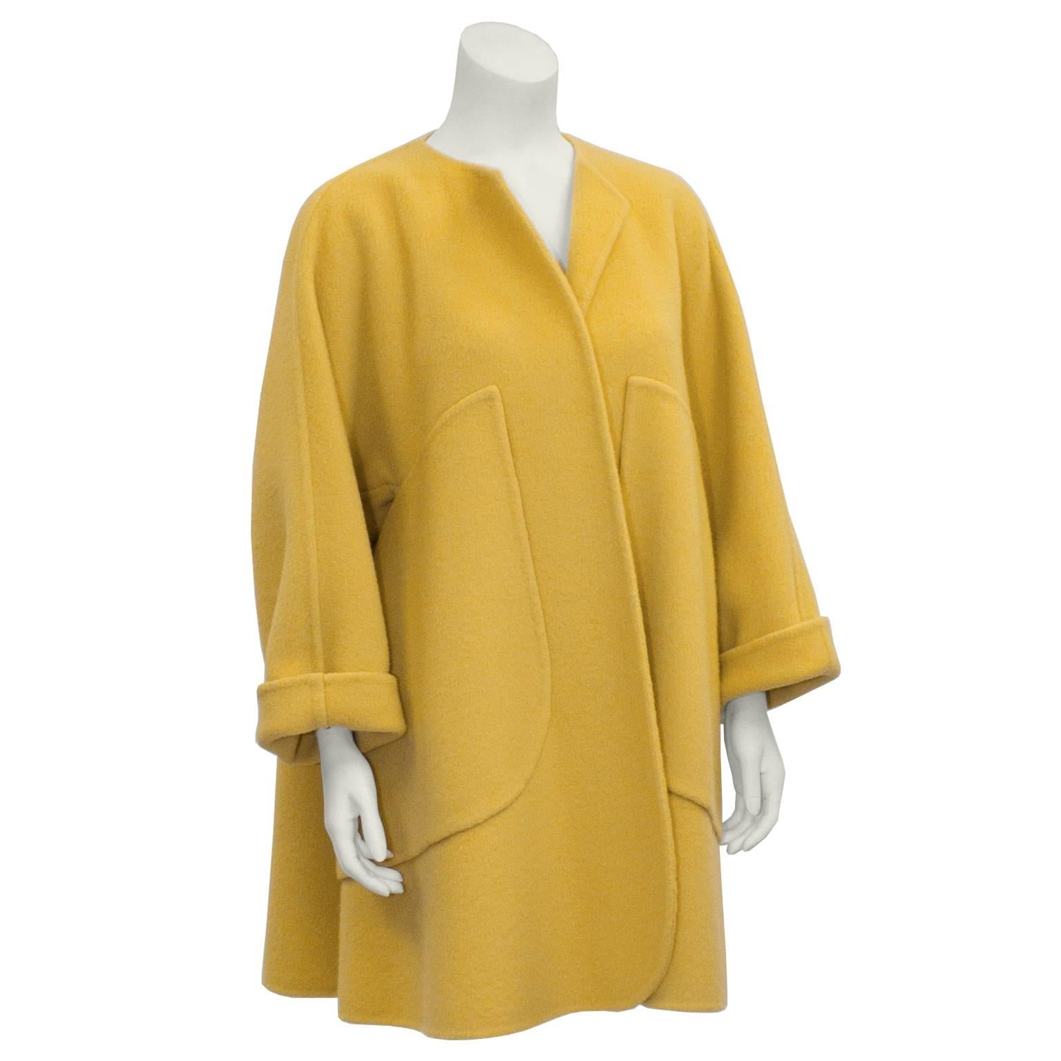 This fabulous Bill Blass mustard color boiled wool swing coat from the 1970's is a classic shape that is generous in fit. Neck is collarless but can be worn with a slight turn back. Sleeves roll up at wrists. Interesting over-sized angle set pockets