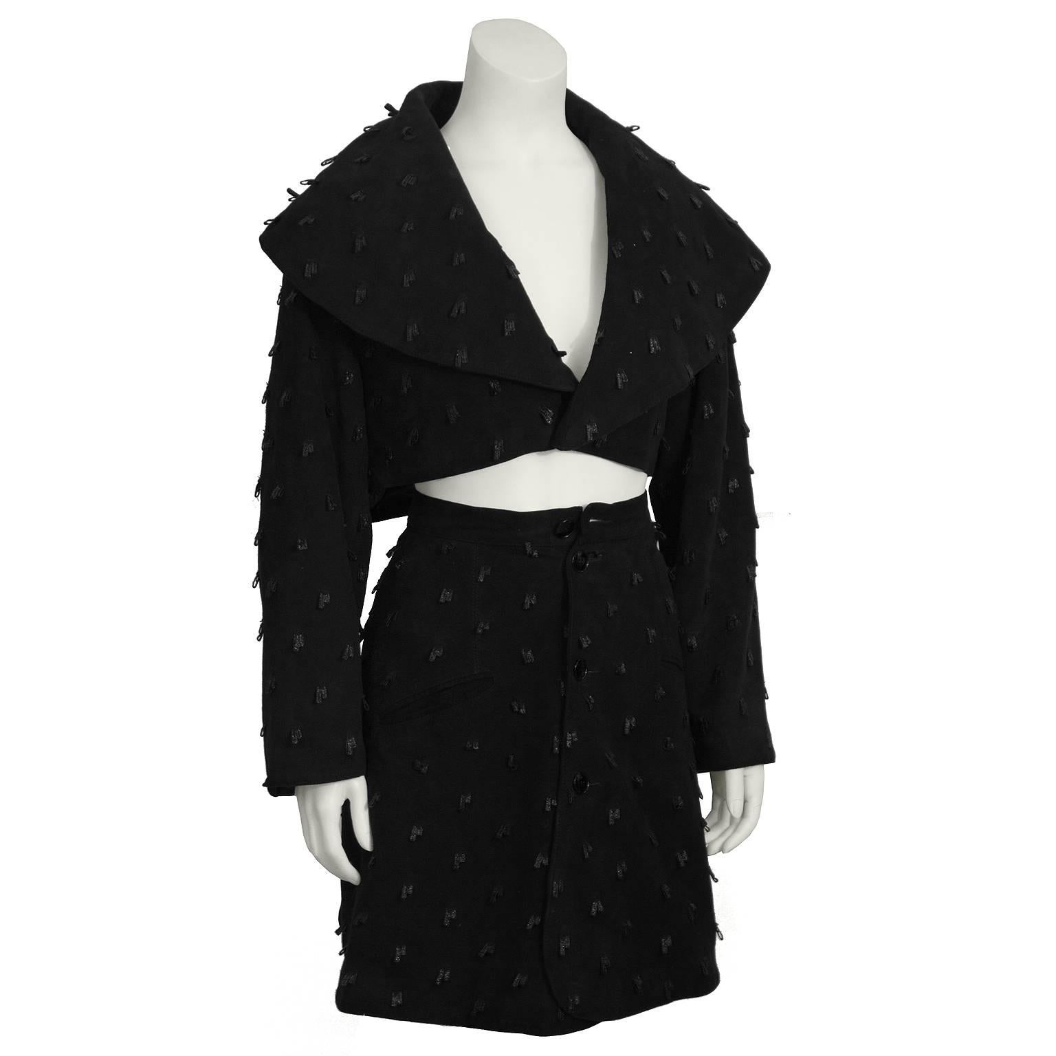This chic Alaia black suede set from the 1980's features a cropped jacket, and mini skirt. Jacket has extended shawl style collar, and single front button closure. A-line mini wrap skirt has two slit pockets at the hips. Front button closure. Unique