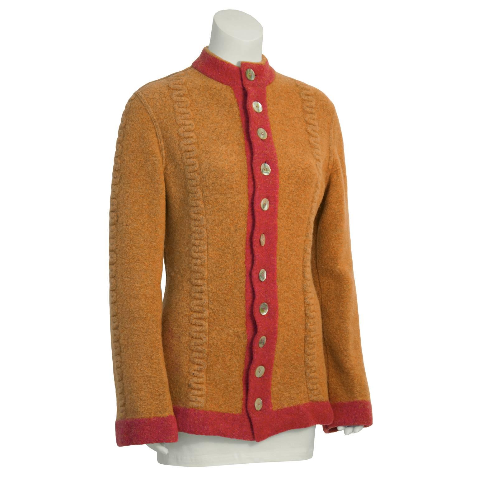 Stay warm and chic with this 1990's Alaia orange wool knit cardigan. Highly sought after early collection piece features orange boiled wool with salmon colored trim, high neck, and cable detail down front. Slightly flared wrists and nipped at the