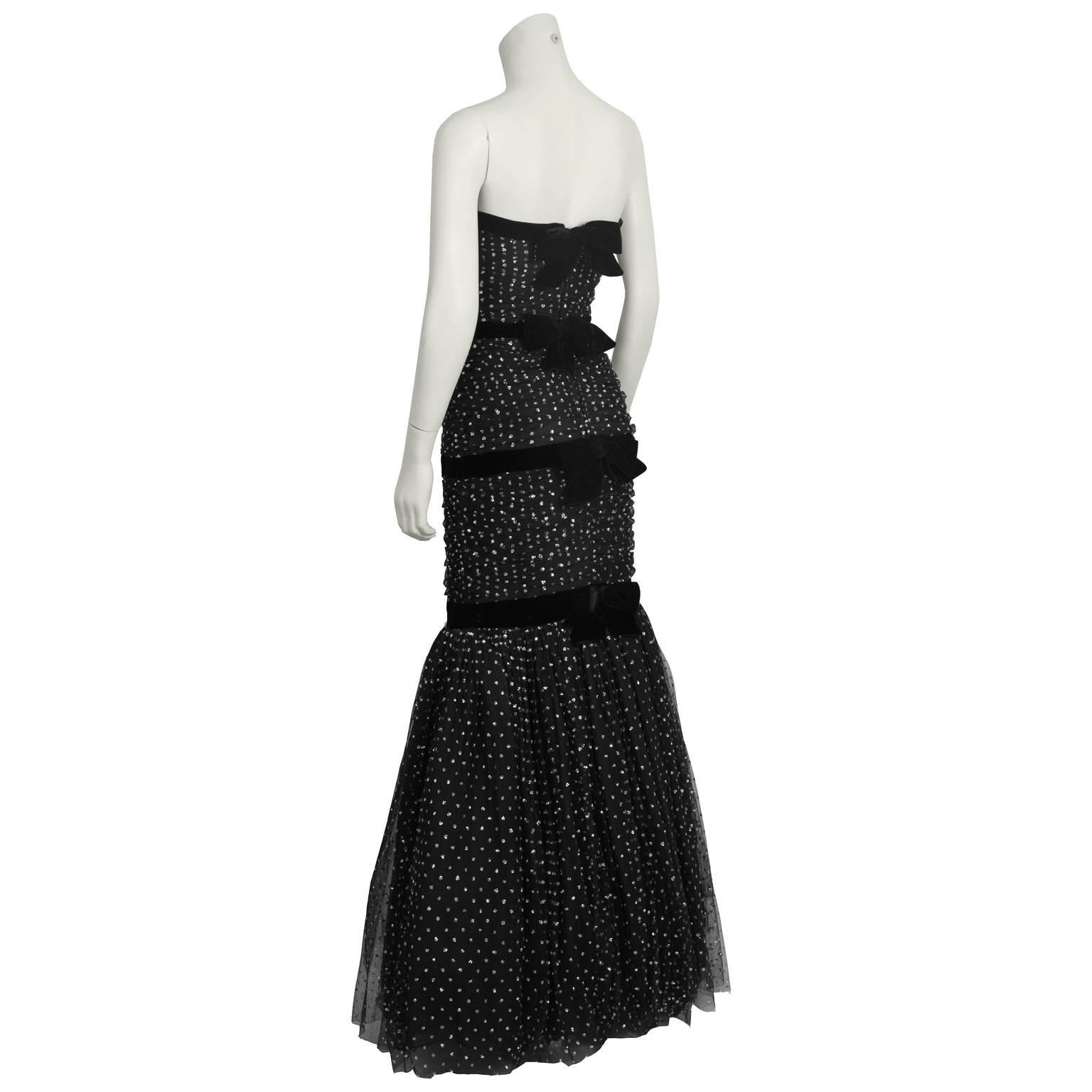 Stunning anonymous black strapless tulle gown from the 1960's dazzles with sparkles throughout. Mermaid cut with ruched black chiffon and a tulle skirt. Three black velvet ribbons trim the top and wrap around the body finishing with bows at the