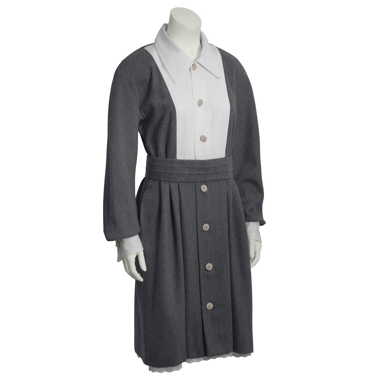 Both modest and adorable, this long sleeve grey wool dress with a white bib and matching underslip dates from the 1960s. Features white collar, loose fitting grey sleeves with white cuffs underneath. Belted at the waist. Skirt is softly pleated and