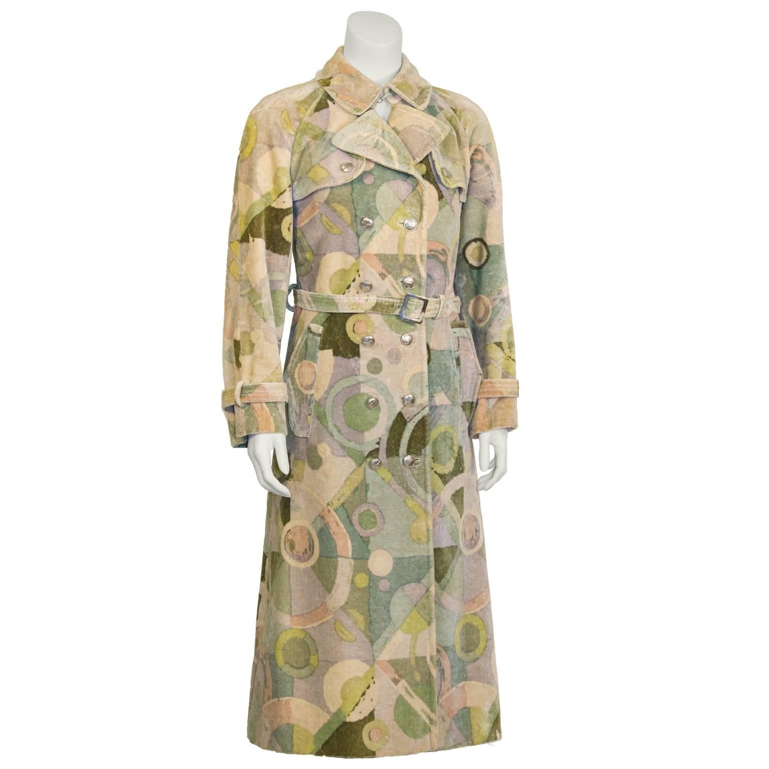 Fabulous 1970's green velvet trench coat featuring an abstract pattern with notes of cream, blue, turquoise and rose. Slightly flared, double breasted coat with storm flaps, two flap pockets, a waist belt, belted cuffs and silver hardware. Silver