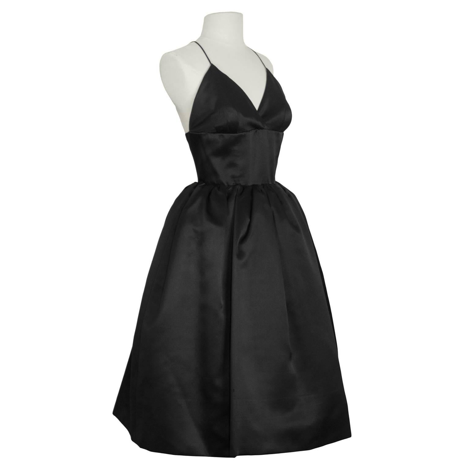 Norman Norell 1950's demi couture for I Magnin black satin cocktail dress with spaghetti strap plunging v neckline. Fitted bodice and pouf skirt with built in crinoline. Straps criss cross in the back, and fastens with two zippers and a waist