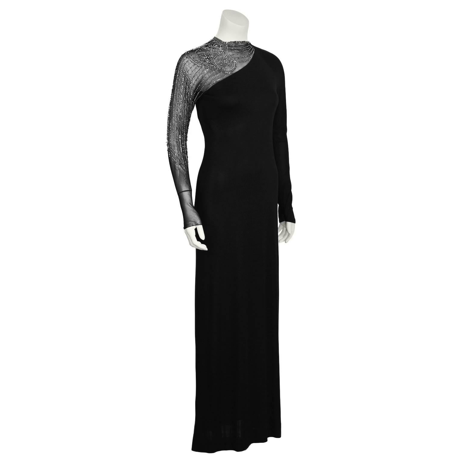 Vestido negro de manga larga de rayón y gasa de los años 50 de Mollie Parnis, con un exclusivo hombro asimétrico de gasa de cizalla y pedrería. El intrincado diseño de cuentas, formado por pedrería y cornetas, cae en cascada por el brazo. Cremallera