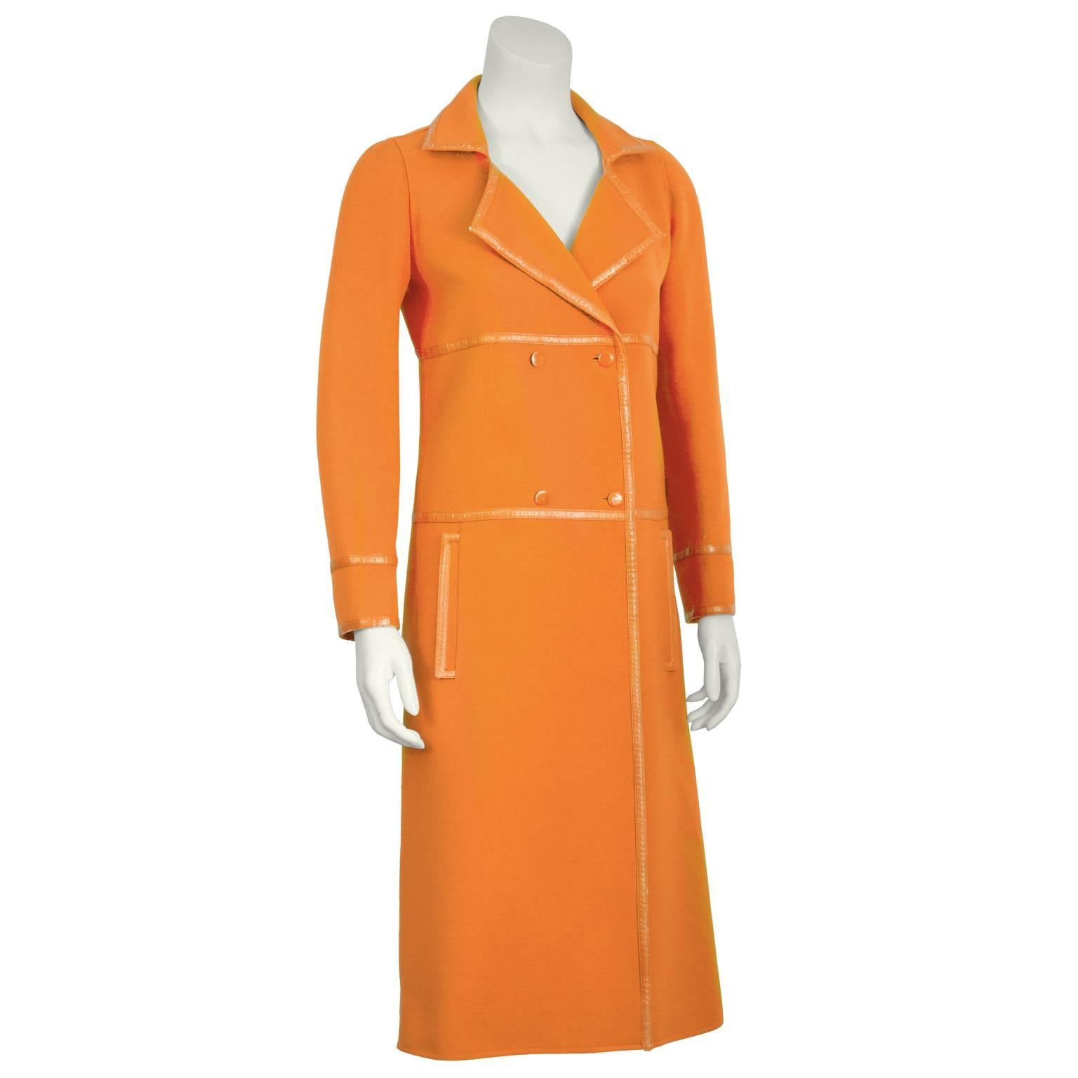 Orange Courreges mod coat from the 1960's features notched lapels, double breasted closure, vertical flap pockets at the hips, and a triple vented panel detailing at the back. Tonal vinyl trim throughout. Some minor flaking to the vinyl