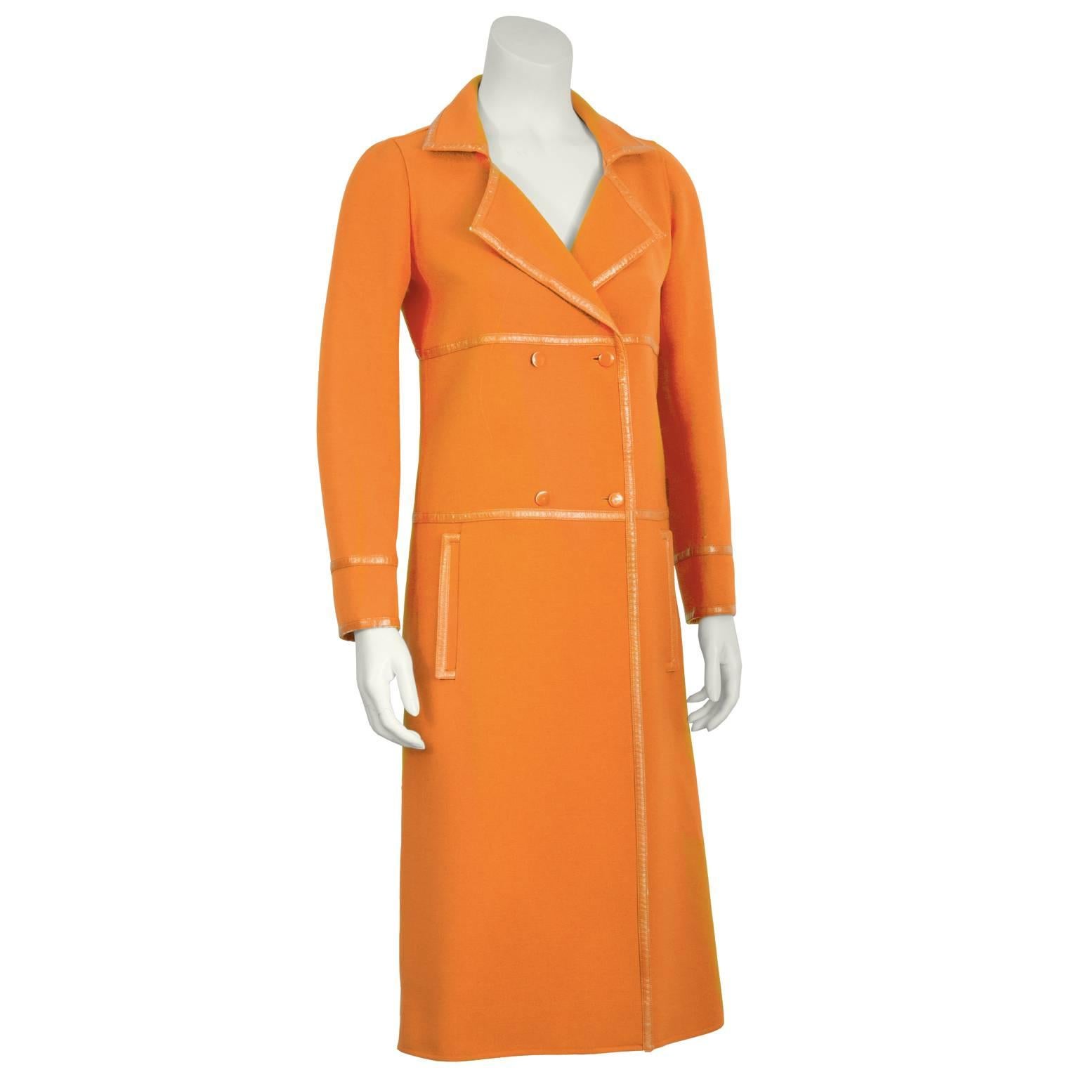 Der orangefarbene Courreges Modemantel aus den 1960er Jahren hat ein gekerbtes Revers, einen doppelten Brustverschluss, vertikale Pattentaschen an der Hüfte und eine dreifach geschlitzte Rückenpartie. Durchgehend farblich abgestimmte