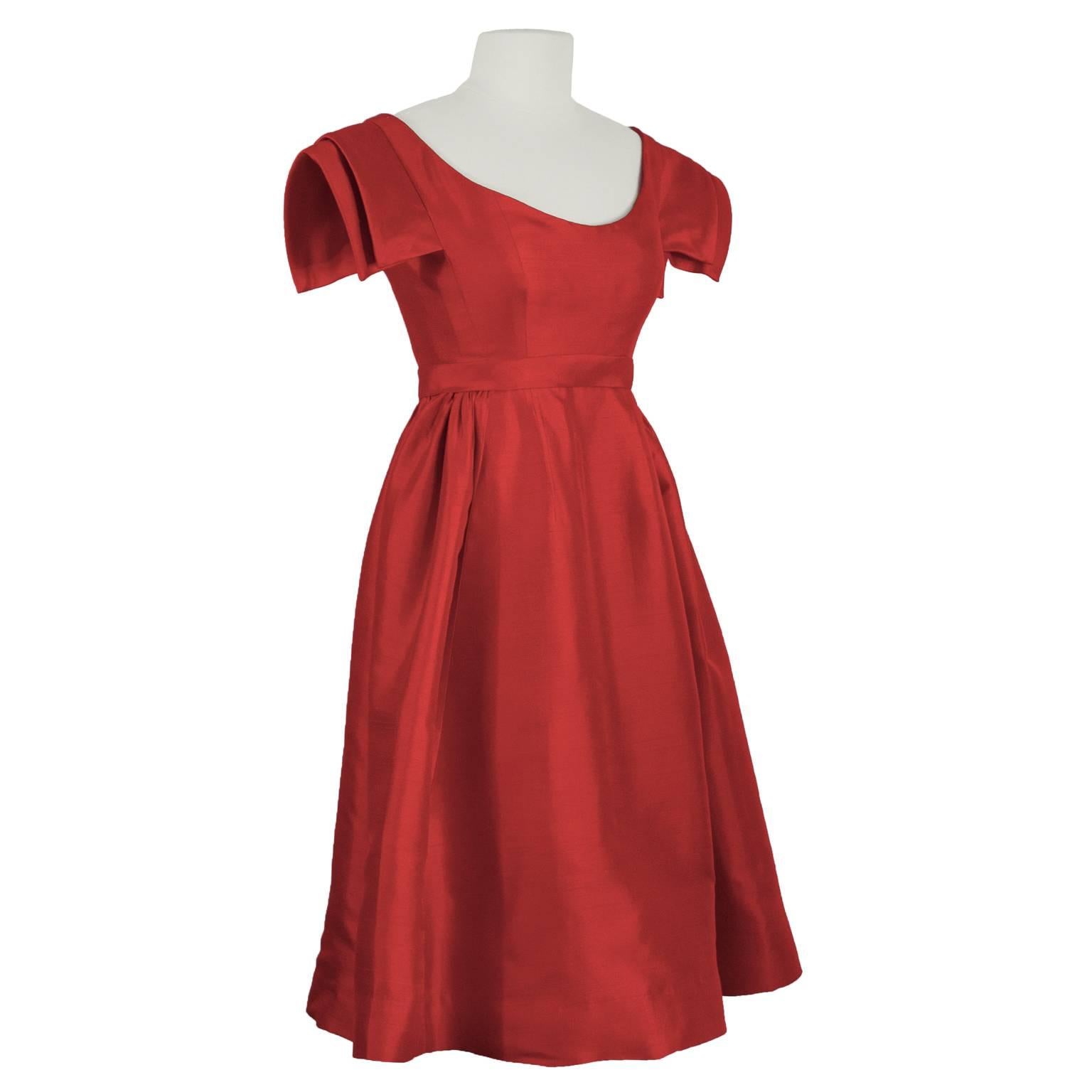 1960's Galanos demi couture iridescent red silk shantung cocktail dress. Features an empire waistline with a scoop neck and double layer structured capped sleeves. Gathering at the sides. Zipper at the back. In excellent condition. Fits like a US
