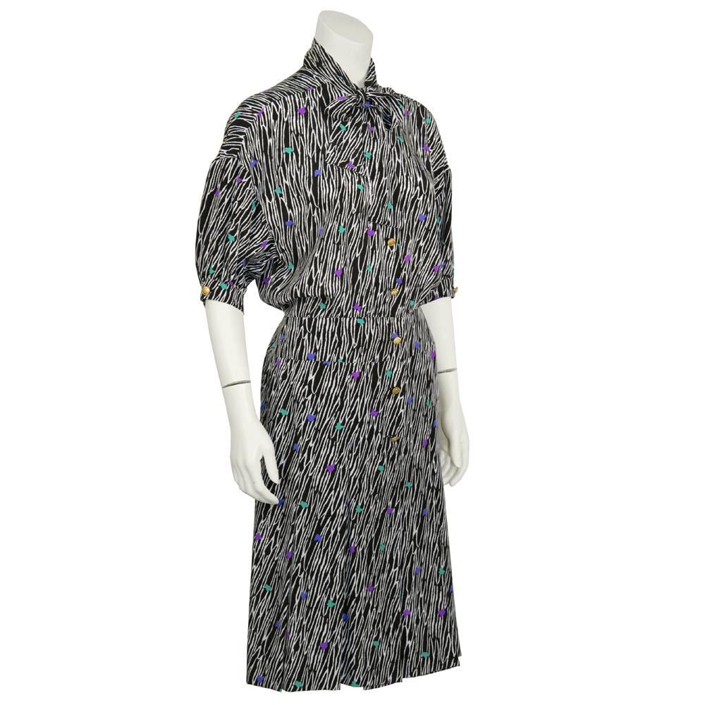 Early 1990's Versace ladies-who-lunch silk day dress made with an allover black and white zebra-like pattern with accents of blue, purple, and green. Features a pussy cat tie bow at the neck, gold buttons down the front, a pleated bottom skirt, and