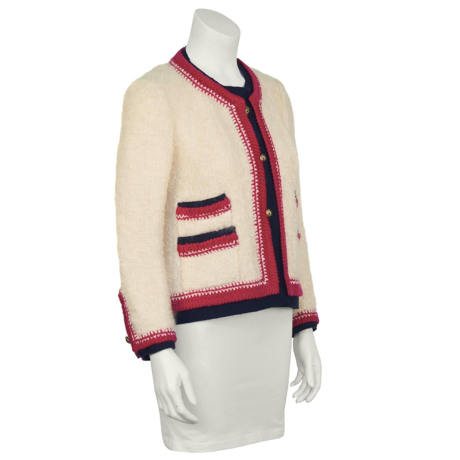 Classic look cream boucle Chanel jacket from the 1980s with magenta and black knit trimming. Feels as comfortable as a cardigan, built like a jacket. Box cut, with two slit pockets on each side and vented cuffs with a button. Fastens up the front
