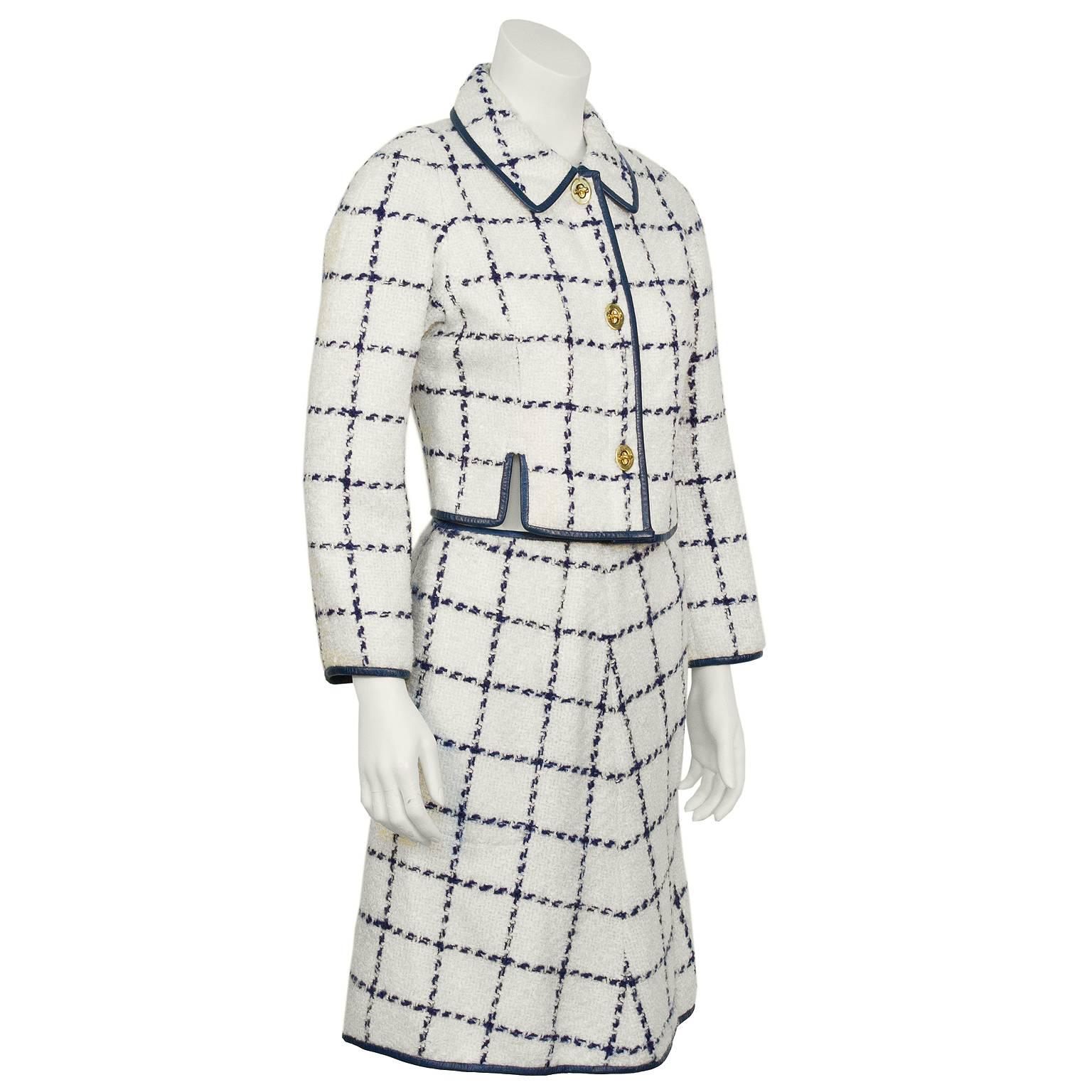 Adorable 1960’s Bonnie Cashin cream and navy windowpane boucle wool suit with navy leather trim. The cropped jacket has a pointed style collar and closes with 3 turn lock closures, made iconic by Cashin and famously used on her designs. The skirt is