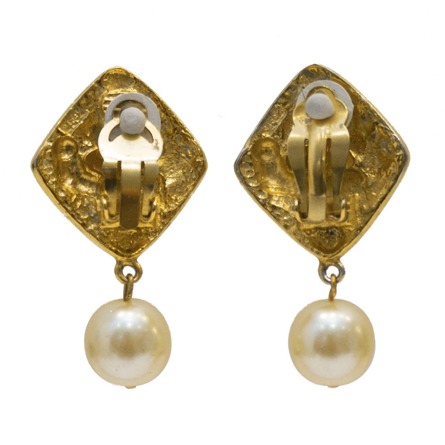 Early 1980's Chanel diamond shaped pearl drop earrings. The clip on style earrings are made up of a gold plated diamond shaped piece decorated with swirl and ball pattern with a small CC at the center. Large faux pearl drop hangs below. In excellent