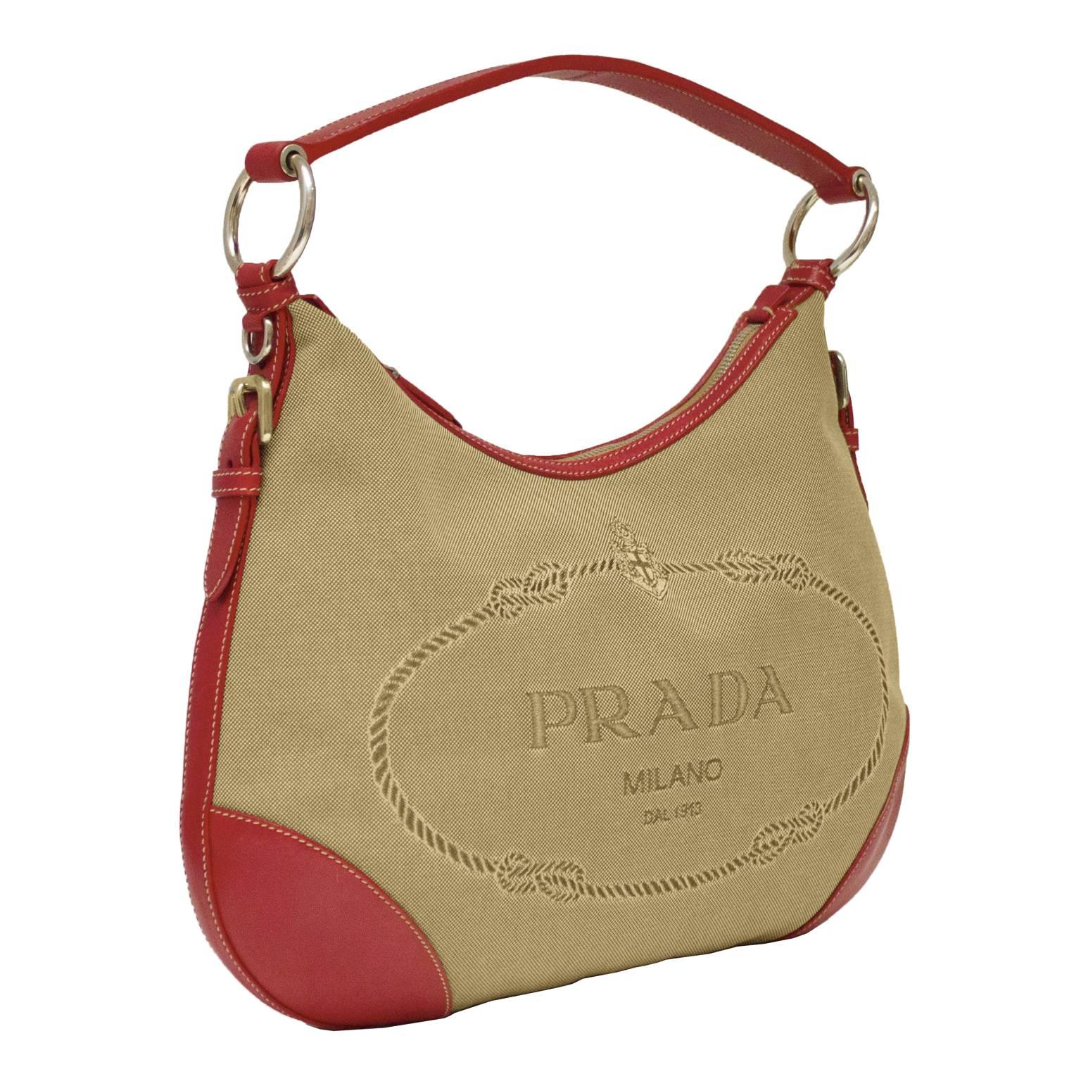 Early 2000’s Prada jacquard hobo style bag with red leather trim. The zip top bag feathers a large crested PRADA MILANO logo woven into the face and is finished with silver hardware. Single zippered interior pocket lined in monogram nylon tone on