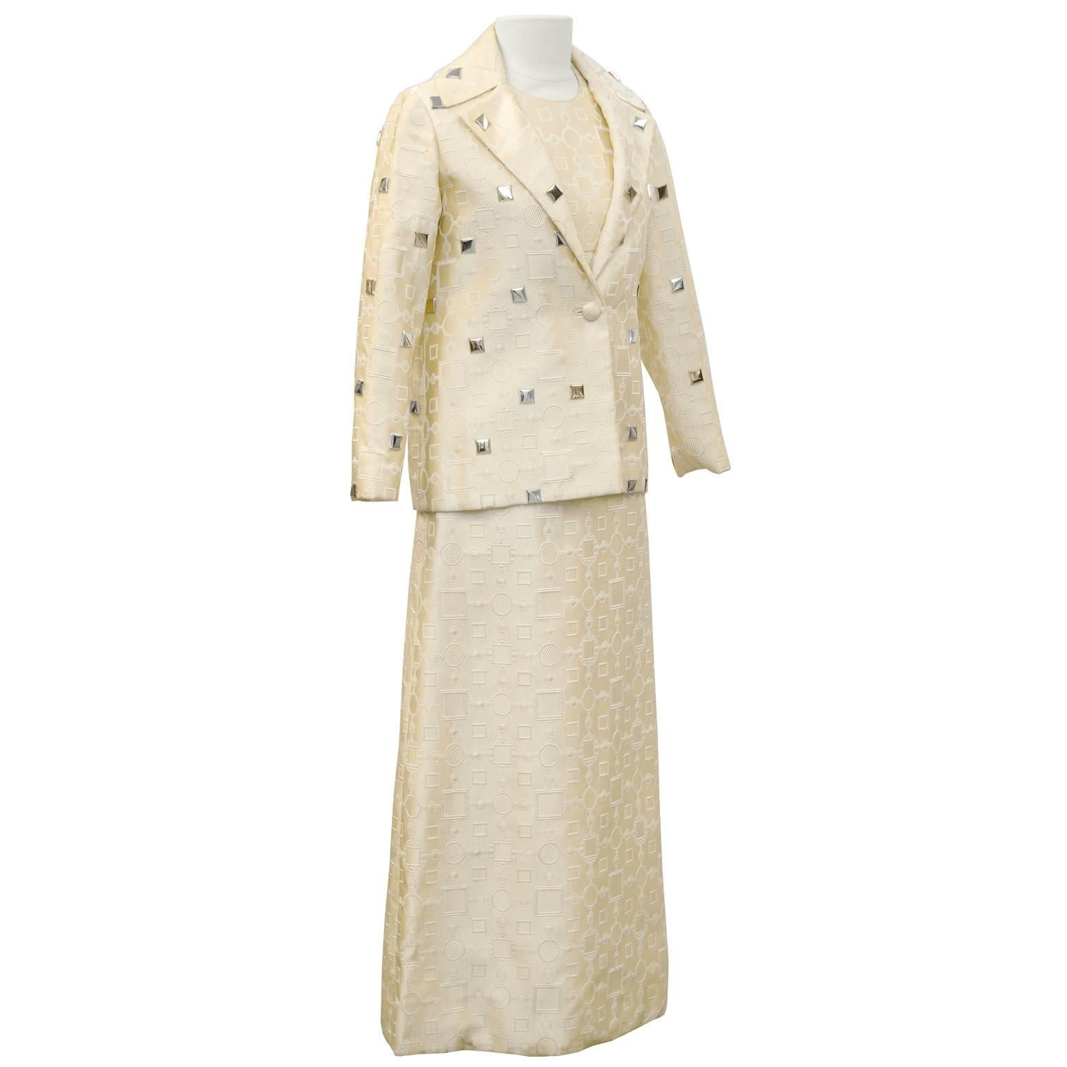 Anonymous cream brocade fabric featuring mod geometric print of circles and squares. High neck empire waist A-line sleeveless gown. Finished with a small notched lapel blazer of the same fabric. Single button closure decorated with gold and silver