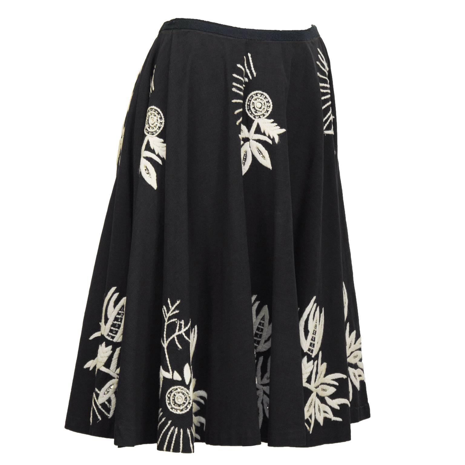 Delightful 1950’s charcoal cotton embroidered circle skirt. Black banded waist, hook and zipper closure on the side. Features cream yarn hand embroidered flower motif with silver pallette details. Unlined. In very good condition. Fits like a US size