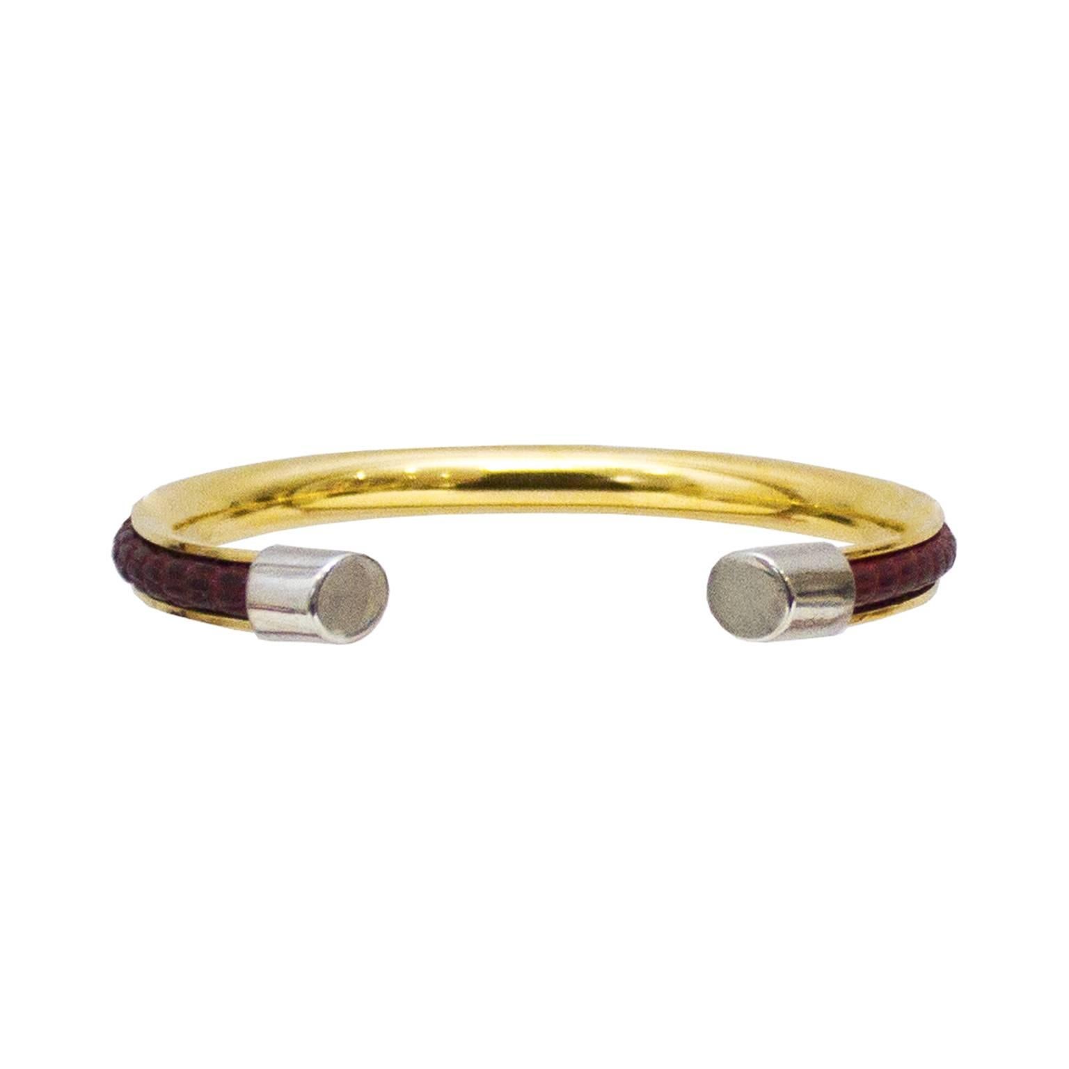 Gucci lizard and gold hardware rigid bracelet from the 1970’s. The burgundy lizard skin is set in a gold tone frame with a Gucci logo engraved in the front and finished with silver tone caps. Stamped “Gucci Made in Italy” on the caps. In excellent