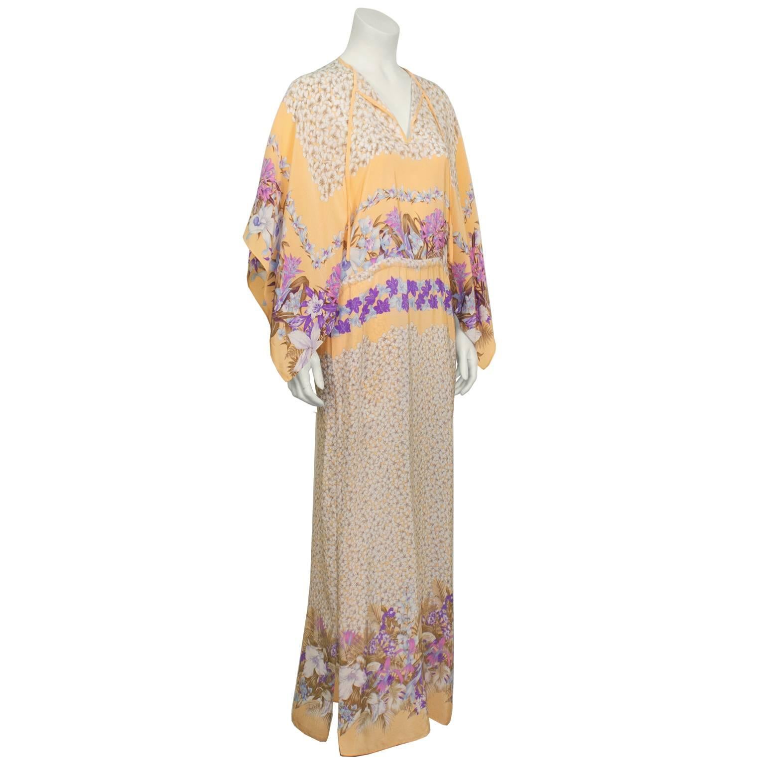 1970’s Marina Ferrari peach floral silk kaftan. The kaftan has a tie-up keyhole neckline, 3/4 length kimono sleeves and a drawstring waist that ties at the side.  The allover floral pattern features cream pansies at the neckline and on the skirt and