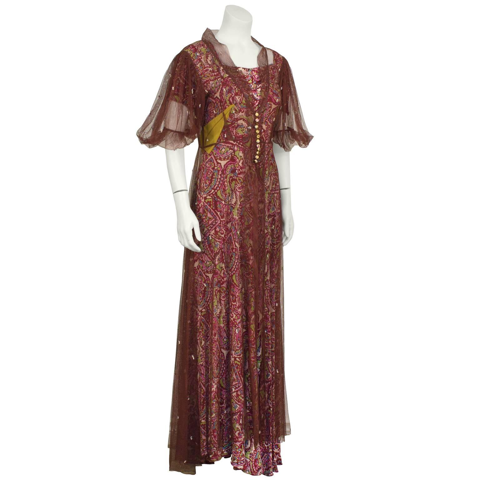 1940's anonymous crepe green and maroon paisley printed gown with attached line green sash that crosses in the front and ties at the back. The matching maroon net overcoat has a puffed short sleeve and fastens at the natural waist with 11 covered