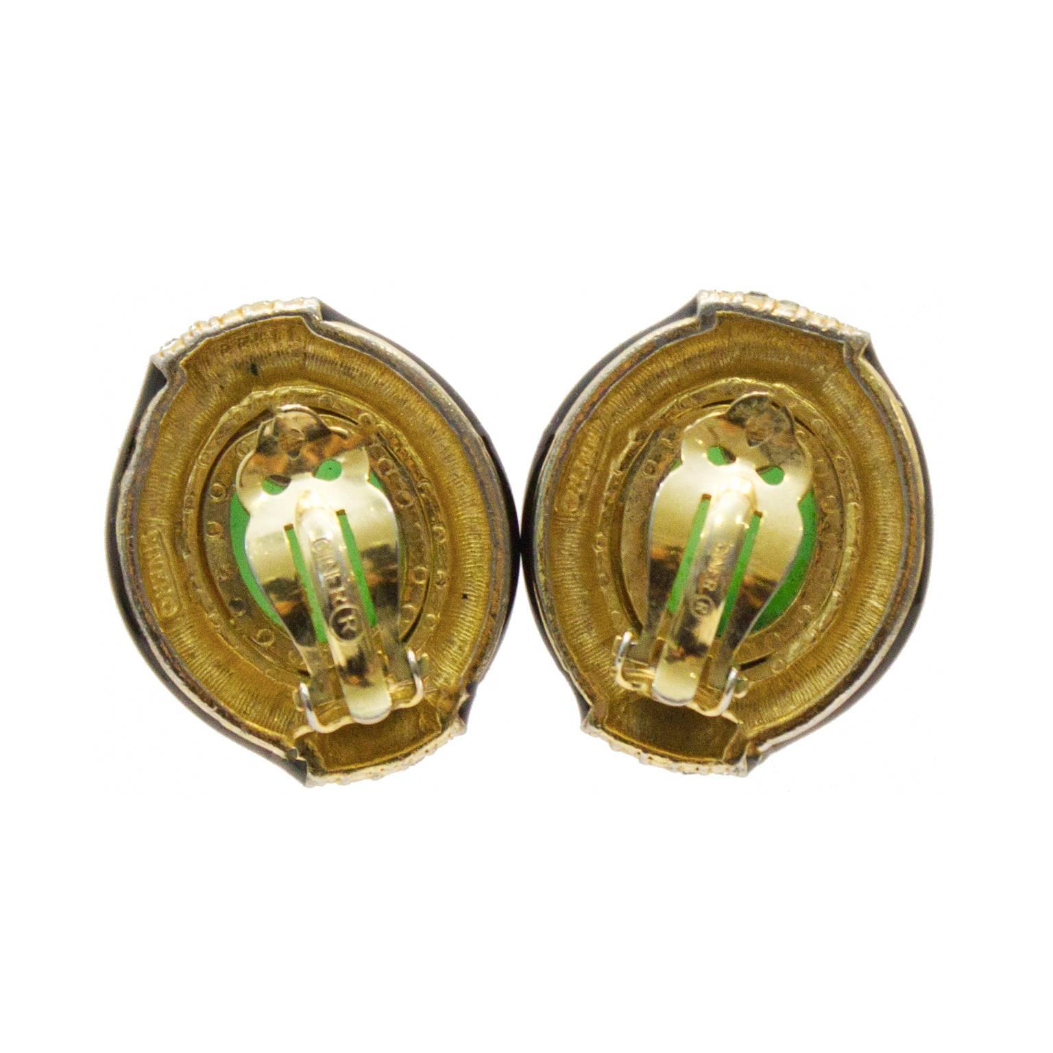 Ciner 1960's poured glass, enamel and rhinestone oval shaped earrings. The clip-on style earrings features a jade-like poured glass cabochon, set in a gold tone hardware, surrounded by a smooth black enamel border with rhinestone encrusted detail.